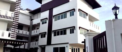 Un moderno edificio residencial de varios pisos con techo plano, ventanas amplias y entrada protegida por una reja.