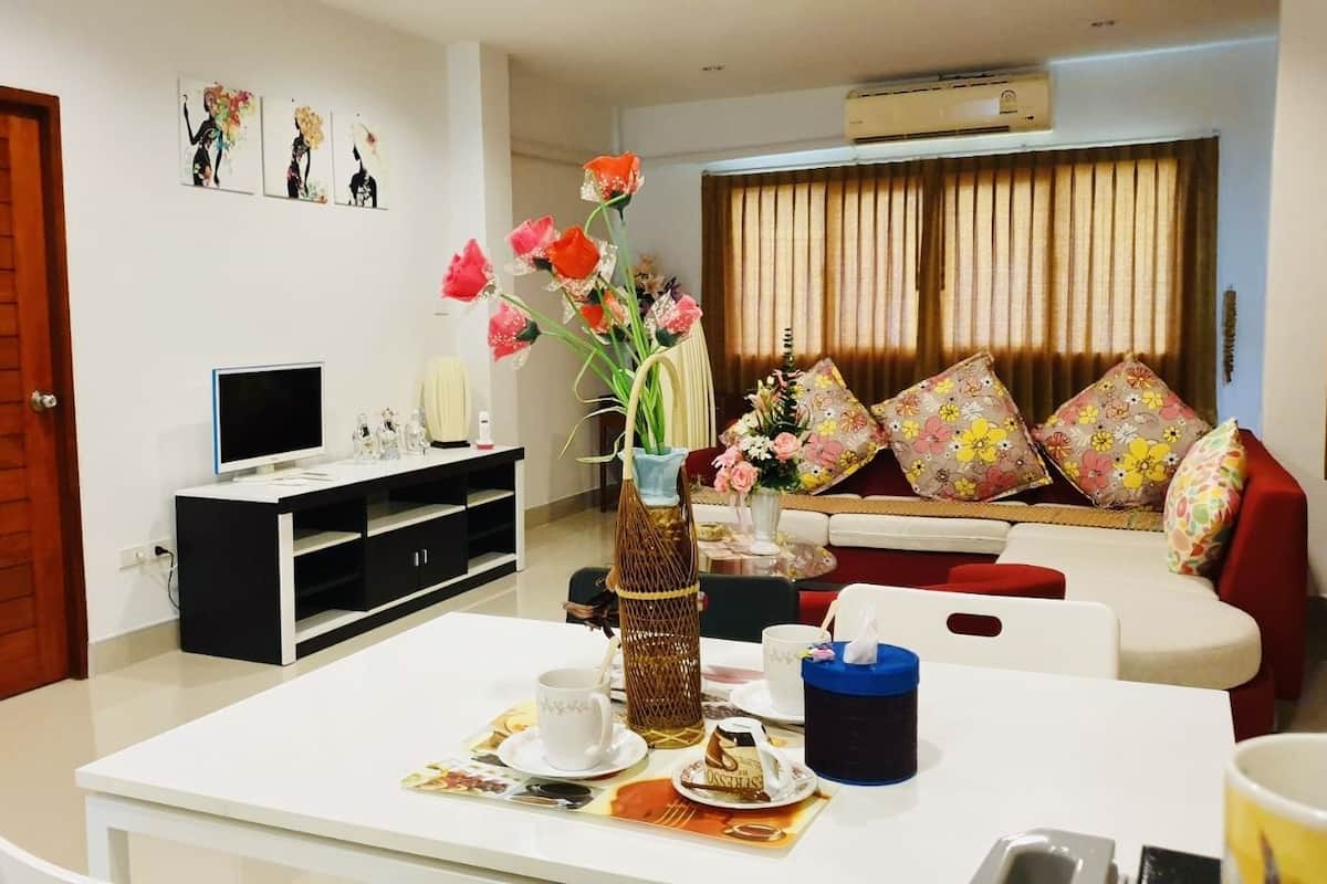 Una sala de estar con un sofá blanco, un televisor y una mesa de comedor con un jarrón de flores.
