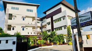 Un edificio moderno de varios pisos con un acceso vigilado, rodeado de abundante vegetación.