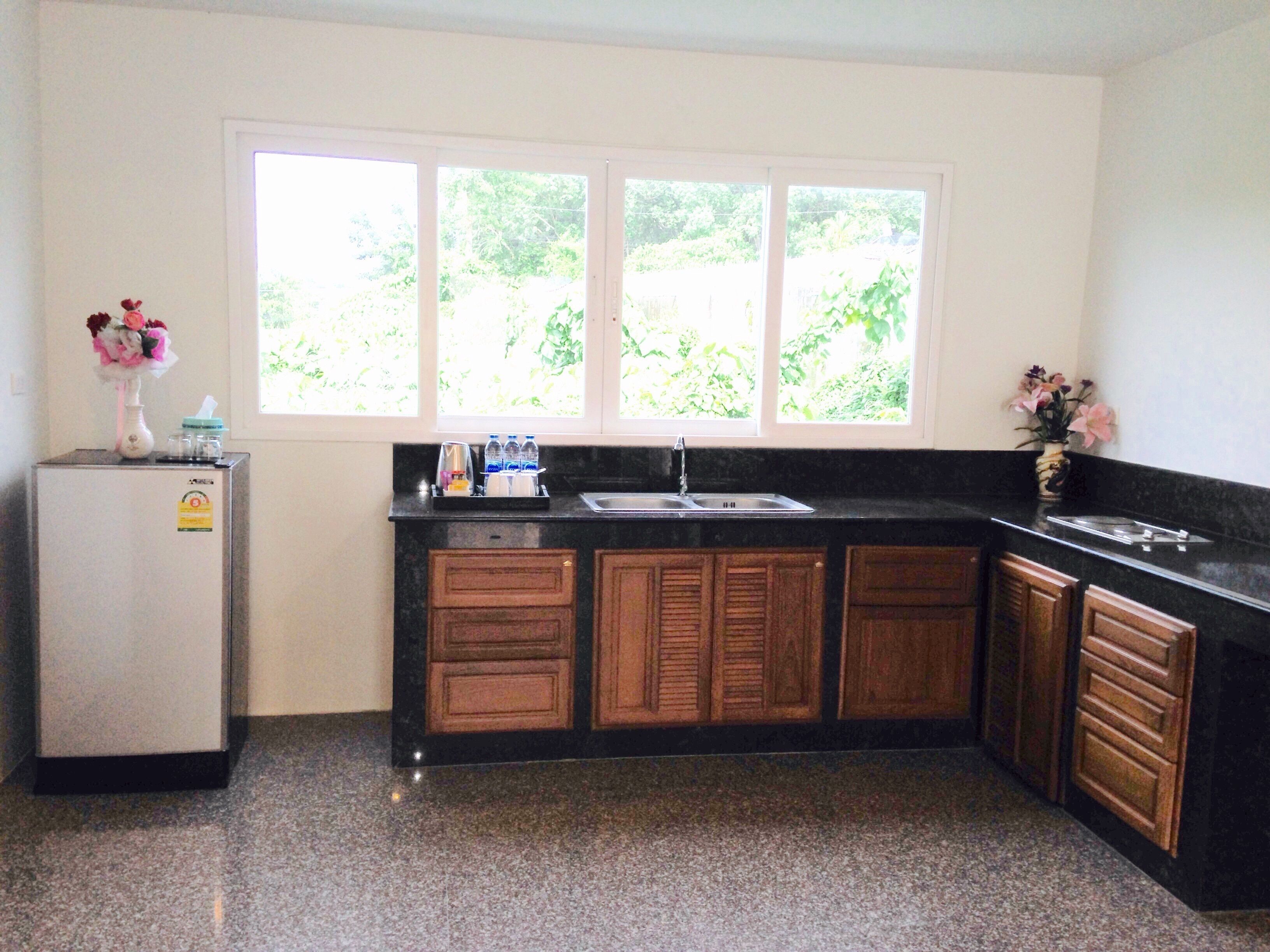 A kitchen with a refrigerator, a sink, wooden cabinets, and a window with a view of greenery.