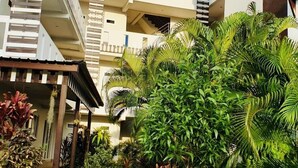 Un edificio moderno con varios balcones, un paseo techado y abundante vegetación.
