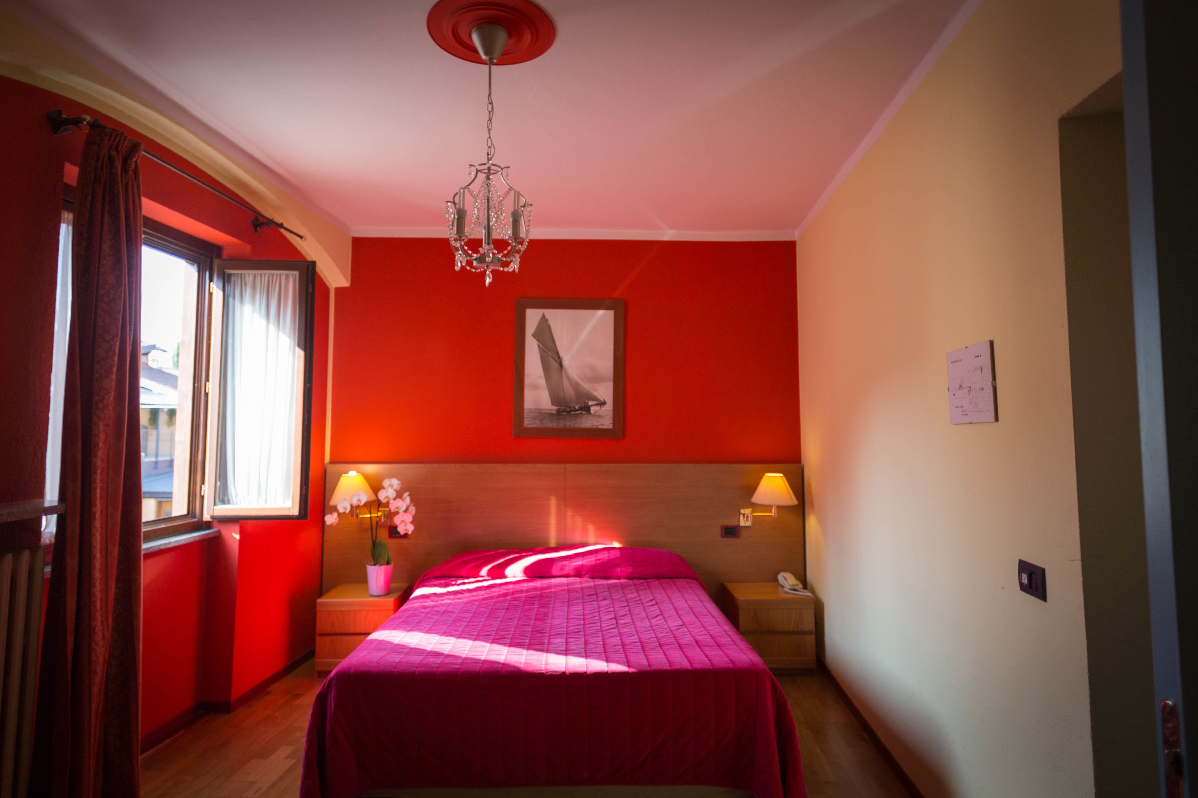 Ein Hotelzimmer mit Bett, Nachttisch, Lampe, einem Fenster mit Vorhängen und einer Deckenleuchte.