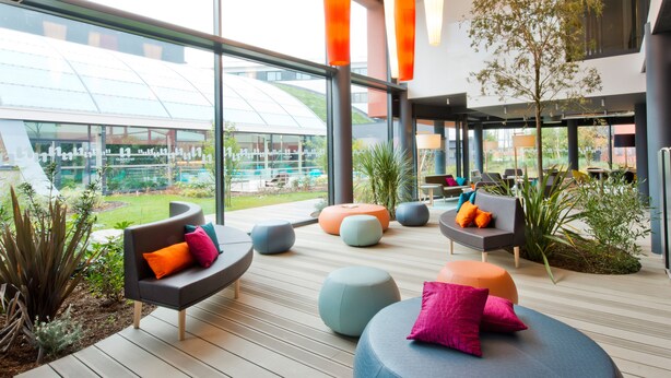 Un espacio interior moderno con zonas de estar, ventanas amplias y plantas de interior.