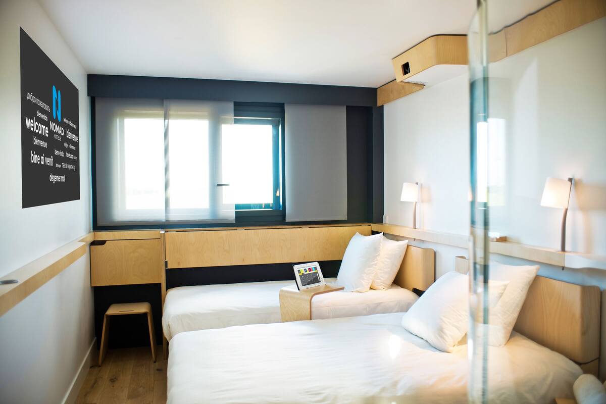 Une chambre d’hôtel avec deux lits, un petit bureau, un ordinateur portable et une fenêtre avec des rideaux.