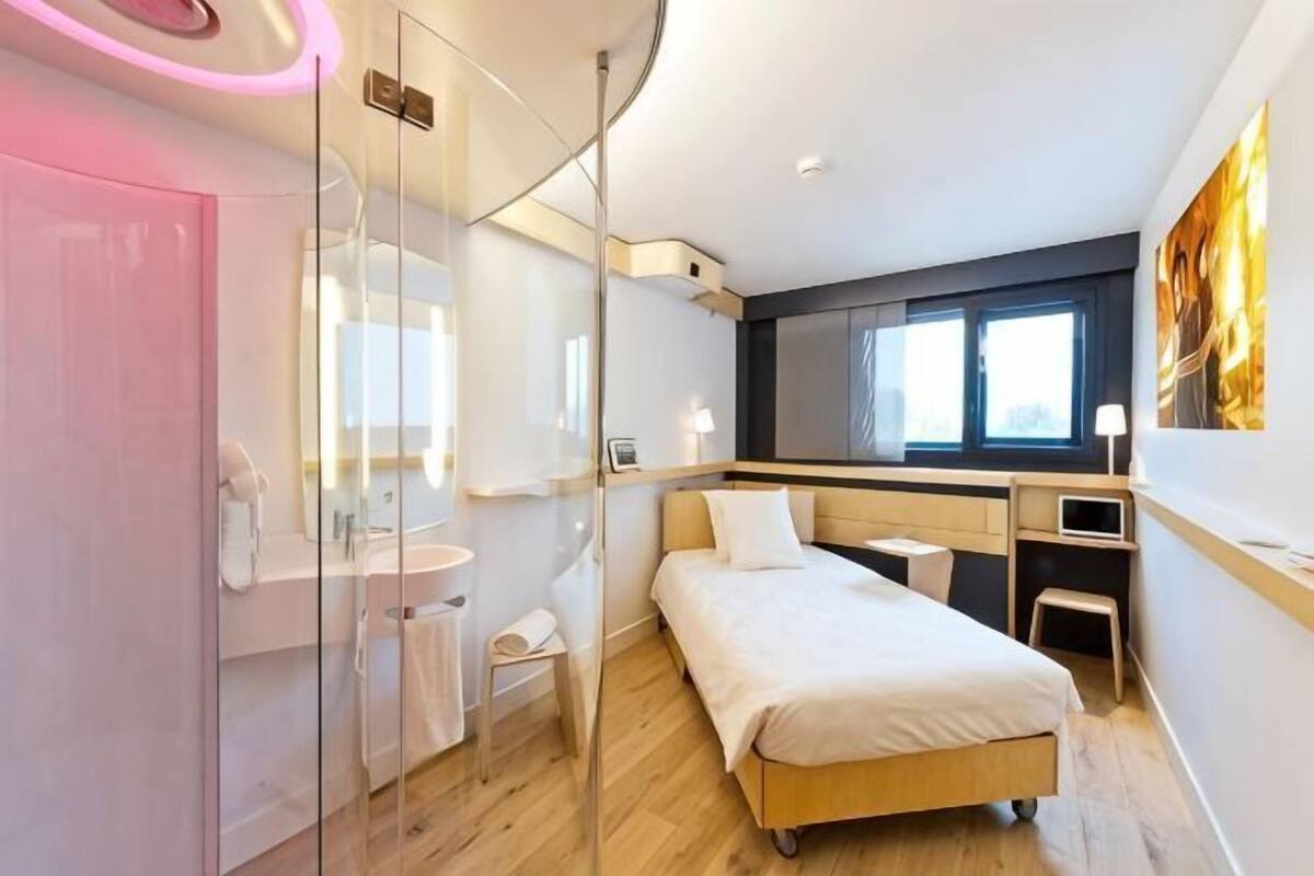 Une chambre d’hôtel moderne dotée d’une douche à parois de verre, d’un lit, d’un bureau et d’une fenêtre.