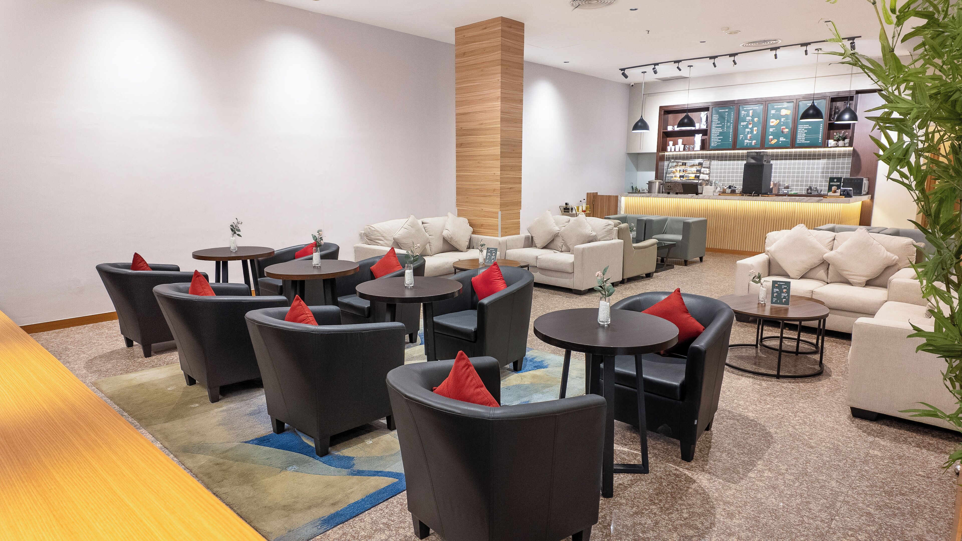 A modern lounge area with sofas, armchairs, and round tables, featuring a bar and a menu display.