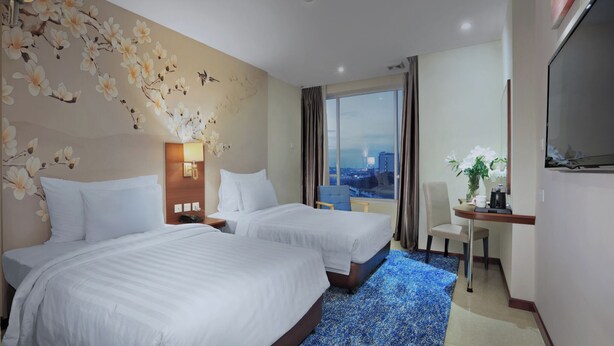 A hotel room with two beds, a desk with a chair, a large window with a city view, and a wall with floral wallpaper. - Aston Inn Gideon Batam (Batam)