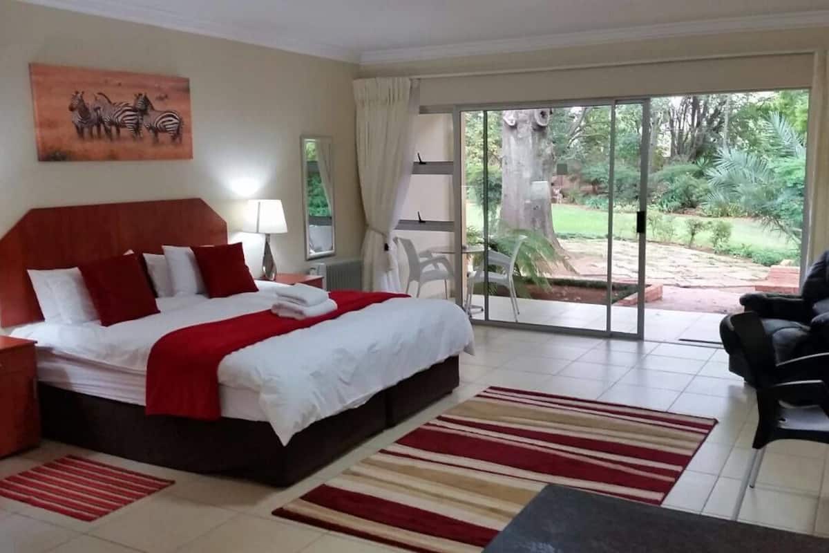 A hotel room with a bed, a desk, a chair, and a view of the garden through the sliding doors.