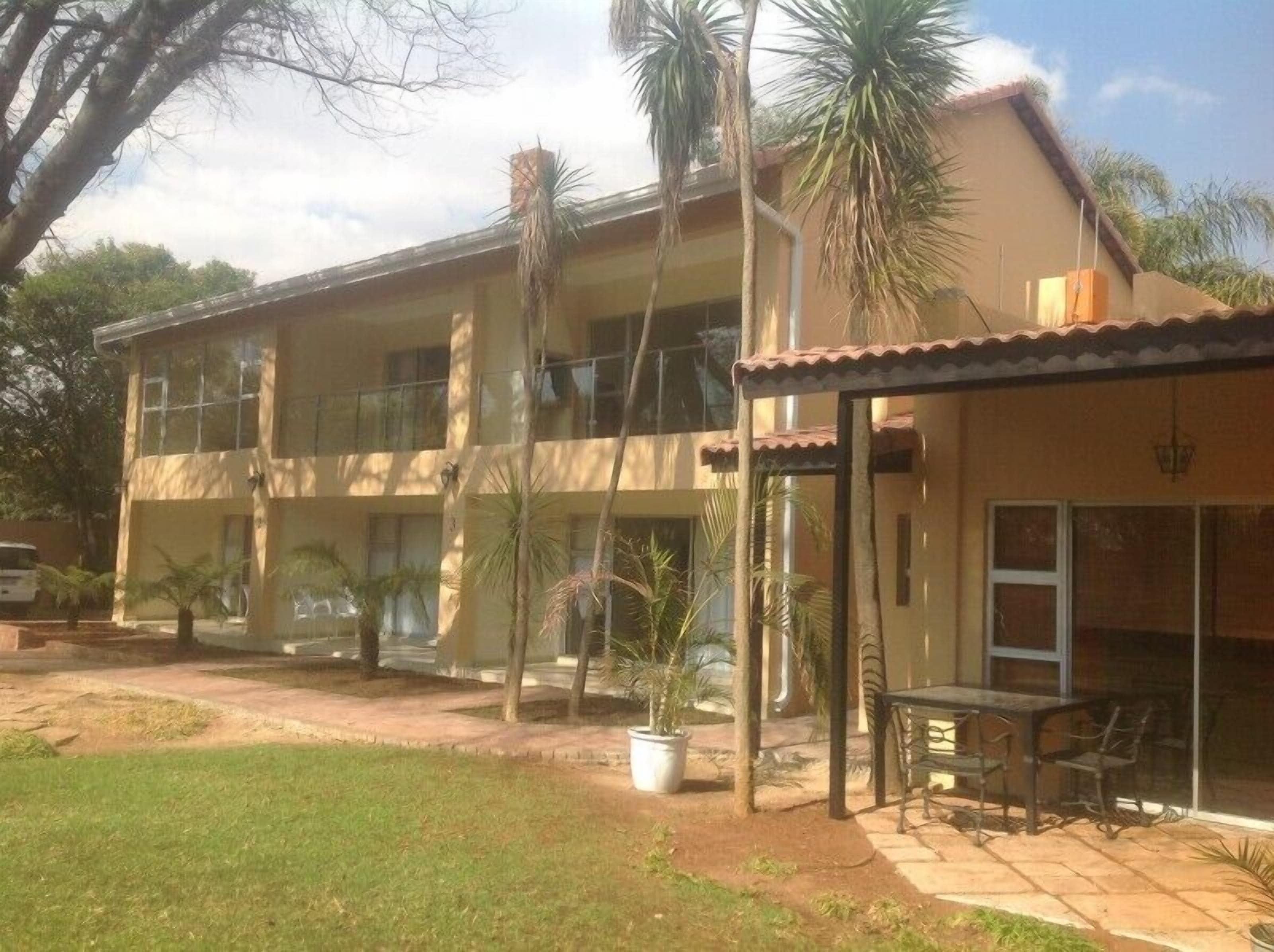 A two-story building with balconies, a covered outdoor seating area, and a garden with palm trees.