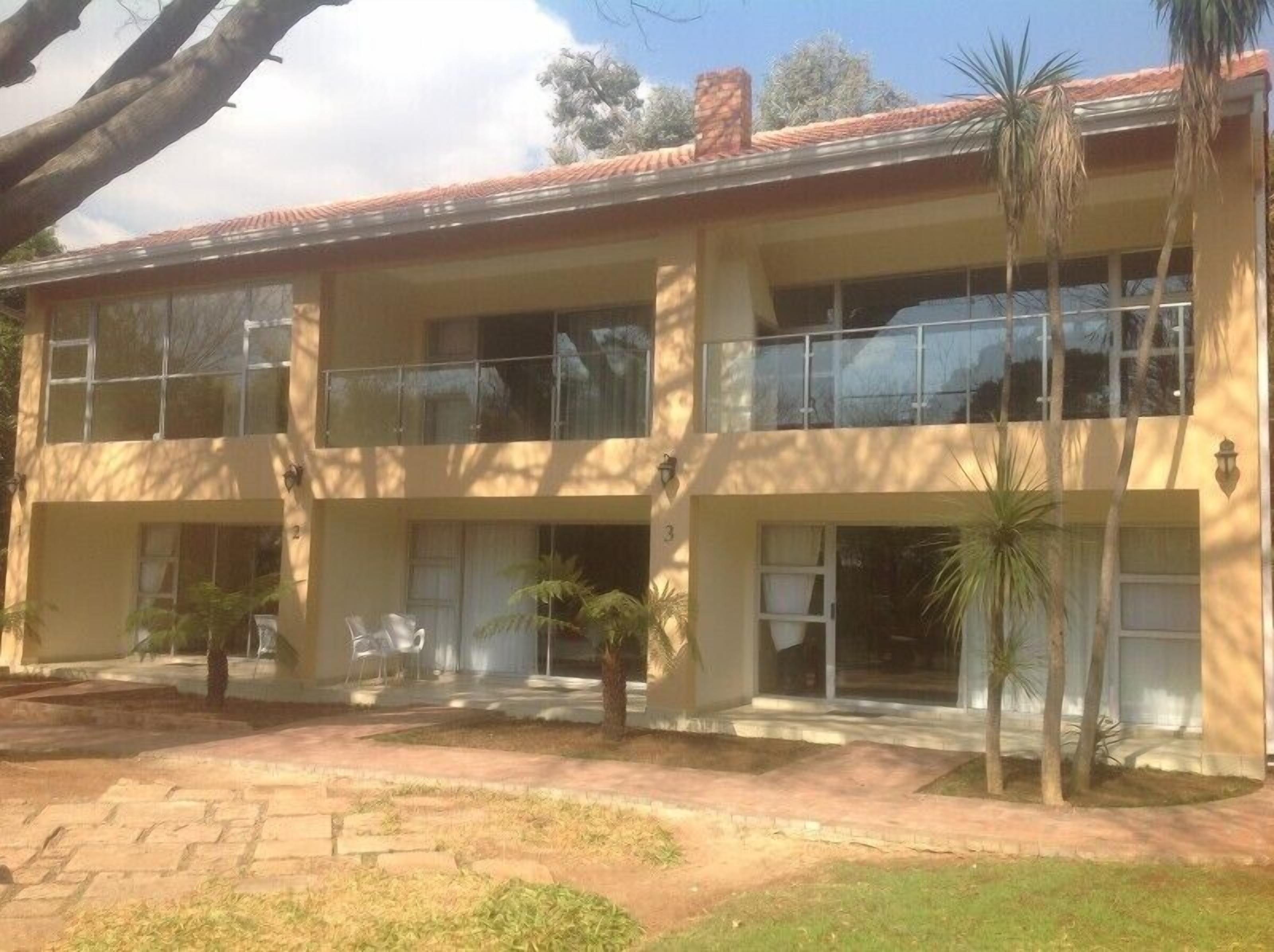 A two-story building with a flat roof, large windows, and a paved entrance area with small palm trees.