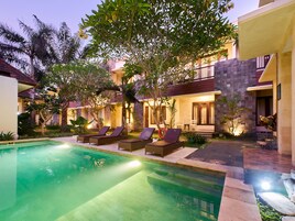 Uma área junto à piscina com espreguiçadeiras, piscina e um edifício com varanda.
