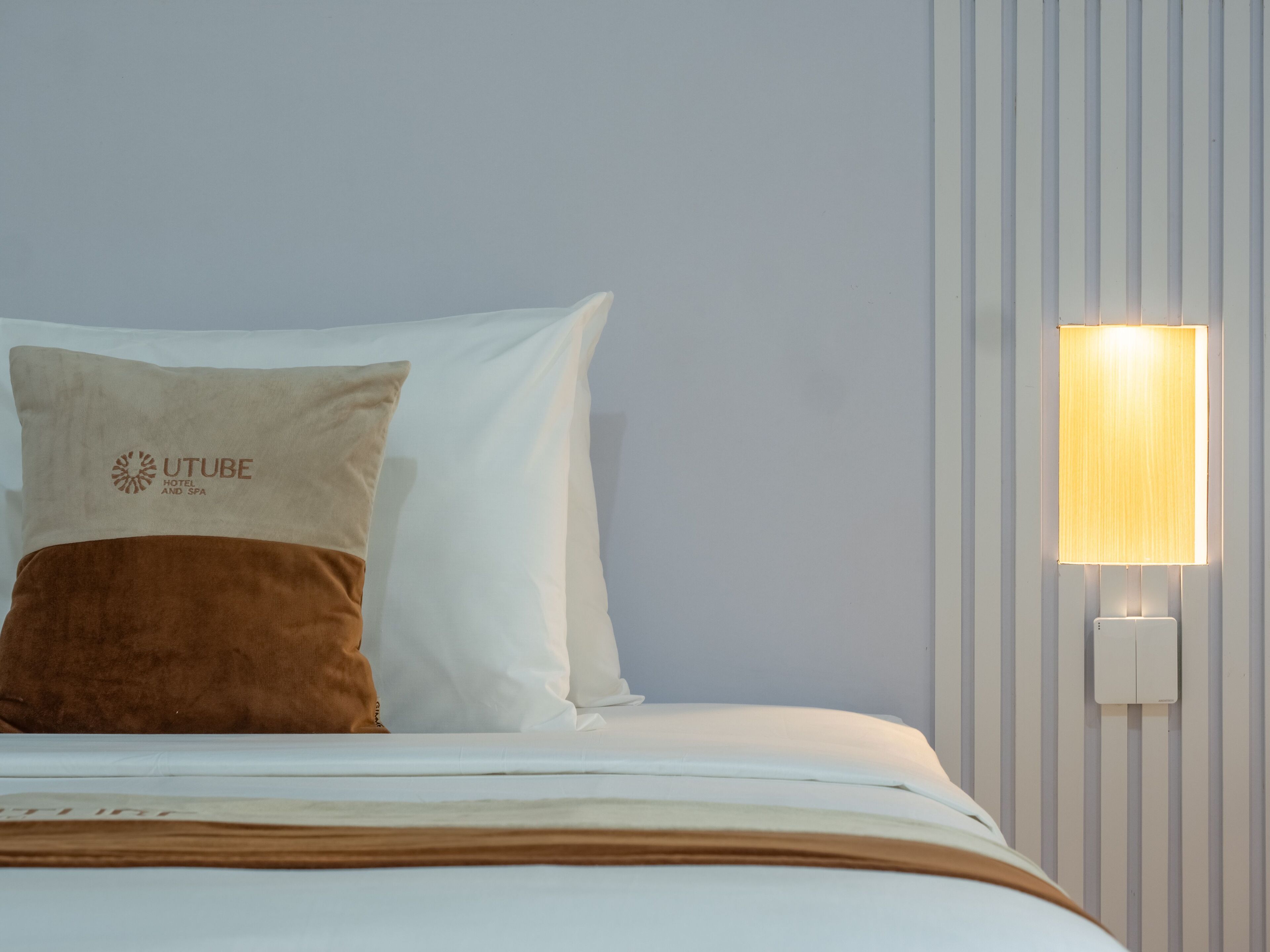 A bed with white and brown pillows, a white blanket, and a wall-mounted light fixture.