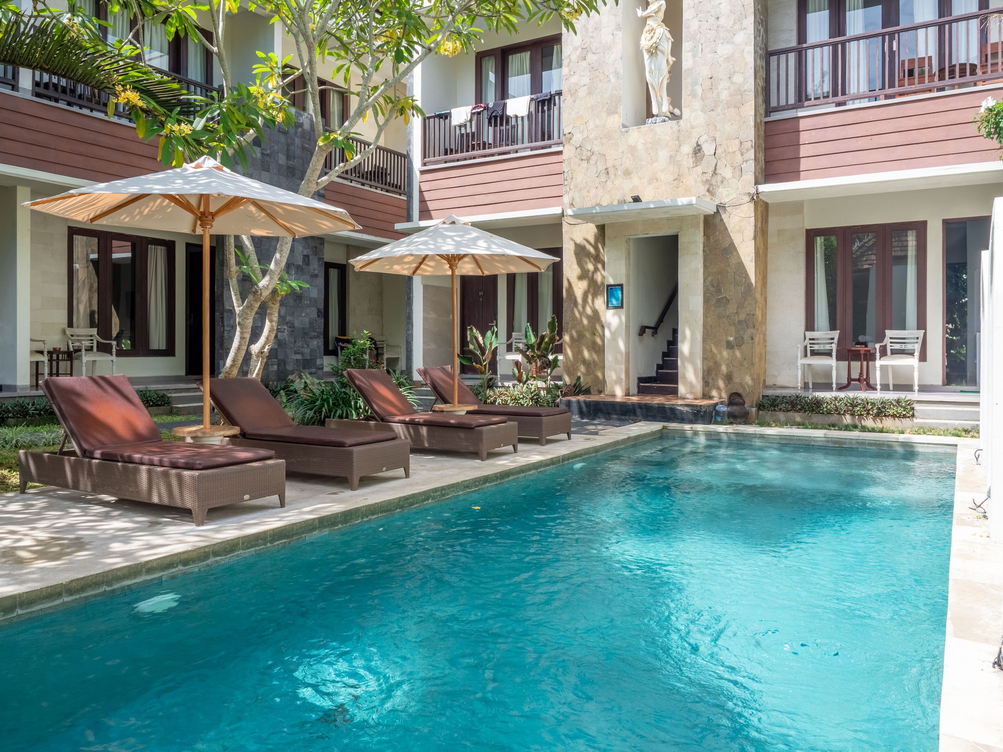 A poolside area with lounge chairs and umbrellas, a stone building with balconies, and a statue.