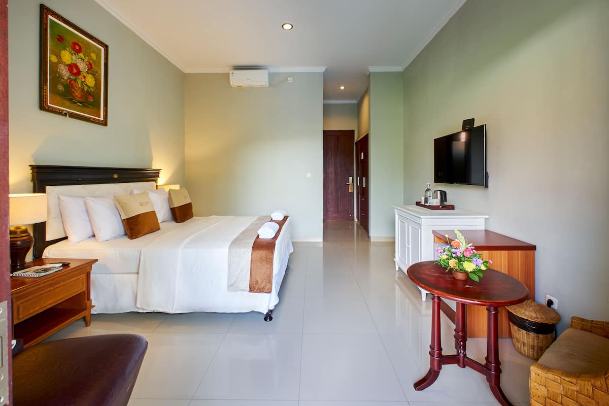 A hotel room with a bed, bedside table, lamp, TV, and a small table with flowers.