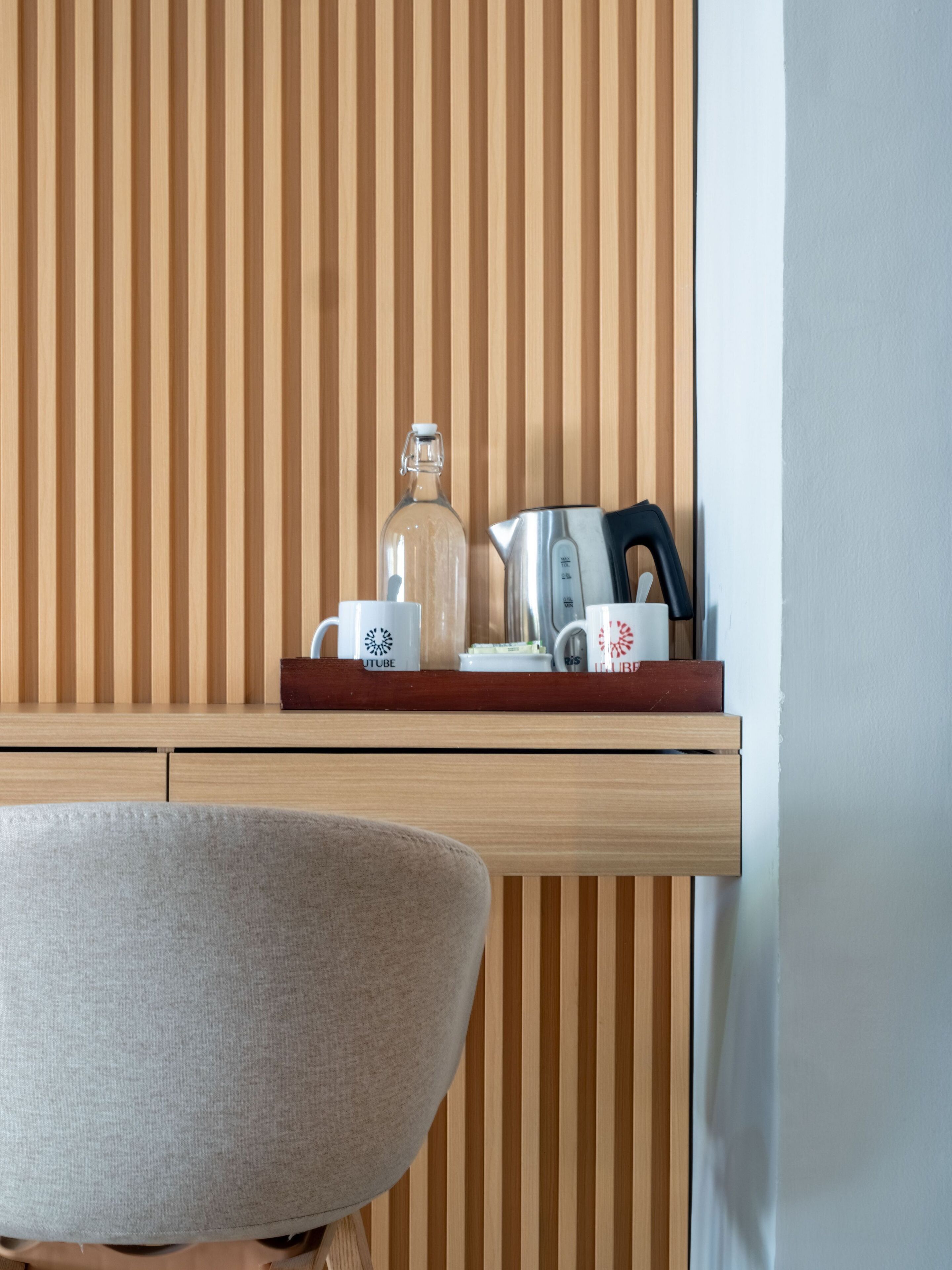 A wooden slatted wall with a shelf holding a glass bottle, a kettle, and two mugs with logos.