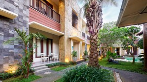 Un edificio de varios pisos con balcón, mobiliario exterior y un jardín bien cuidado con una palmera.