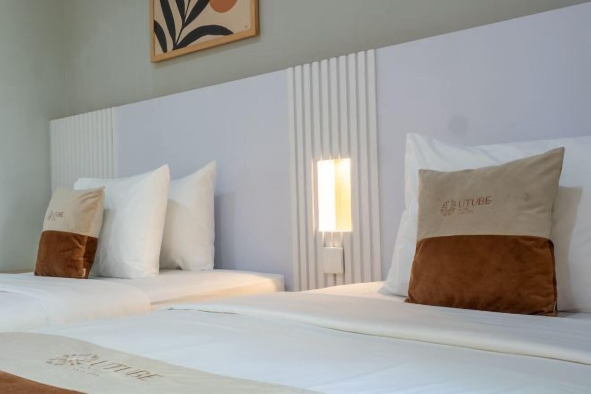 A hotel room with two beds, white bedding, and a wall-mounted light fixture.