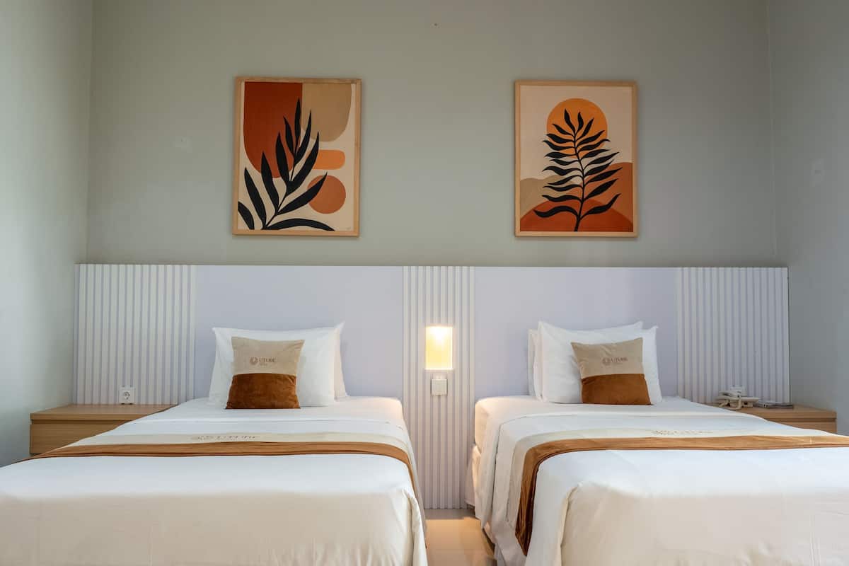 A hotel room with two beds, each with white bedding and brown pillows, a striped headboard, and two abstract paintings on the wall.