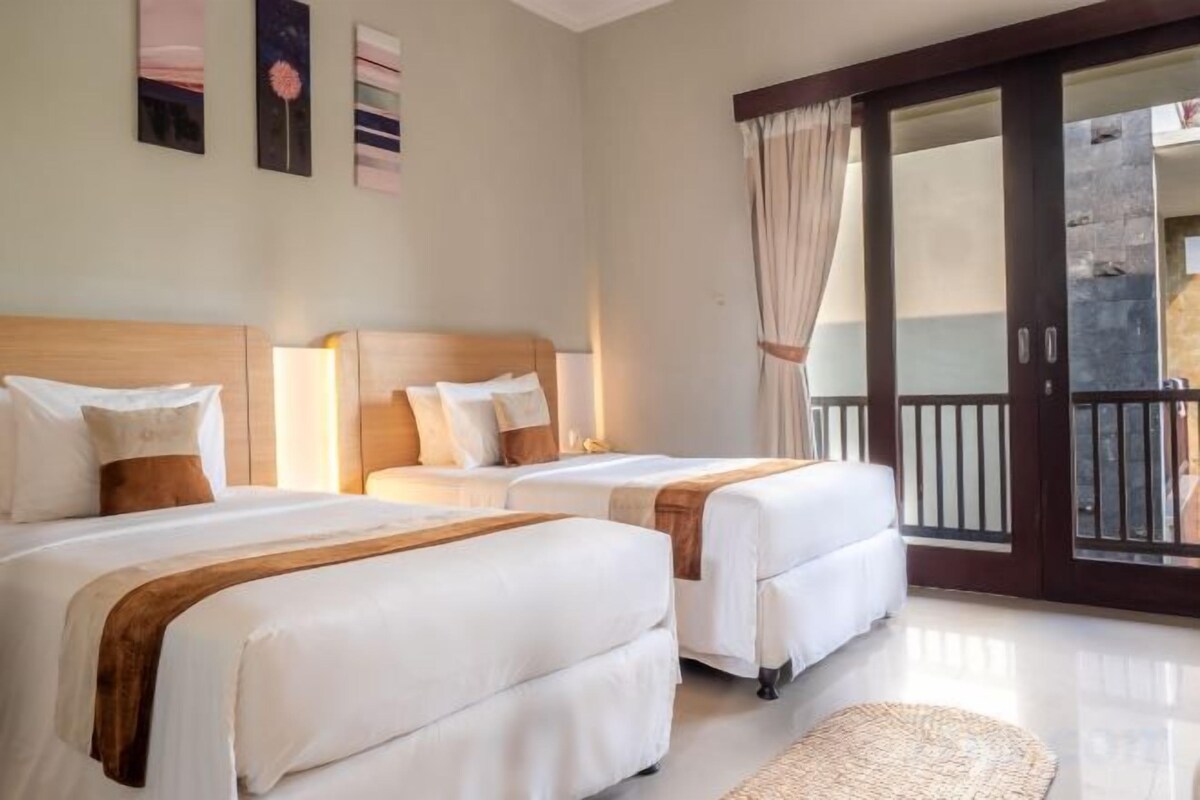 Habitación de hotel con dos camas, un balcón con vistas y una puerta corrediza de cristal.