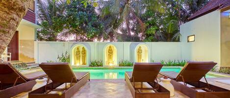 Un área junto a la piscina con sillones de descanso, una piscina y arcos decorativos.