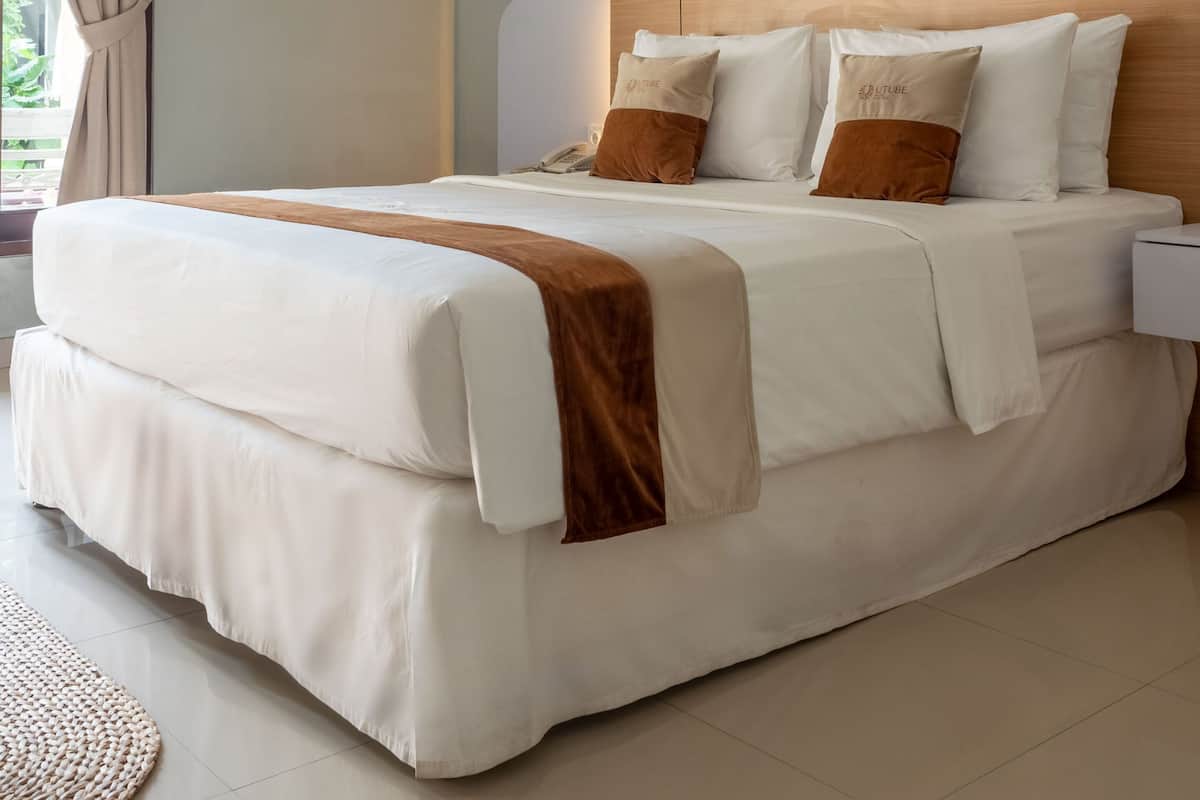 A neatly made bed with a wooden headboard, white bedding, and two brown pillows.