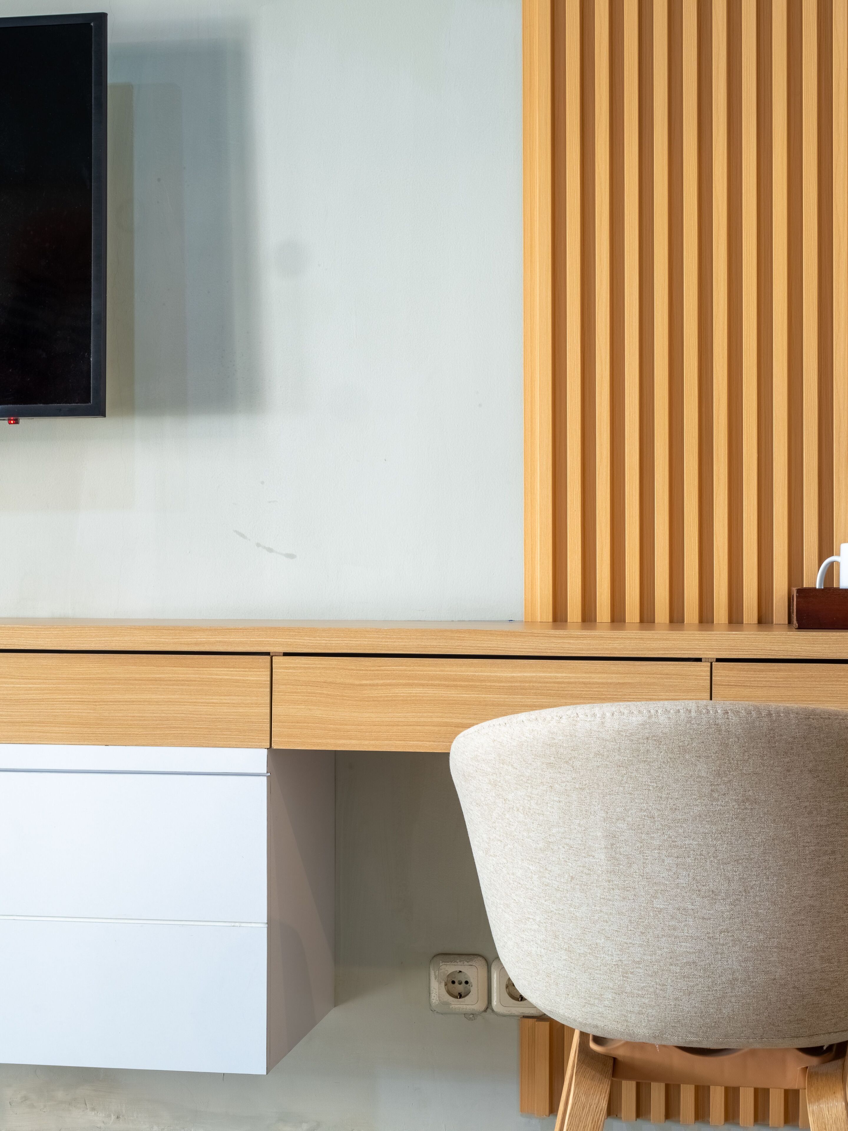 Un espace de travail moderne avec un bureau en bois, une chaise blanche et un téléviseur fixé au mur.