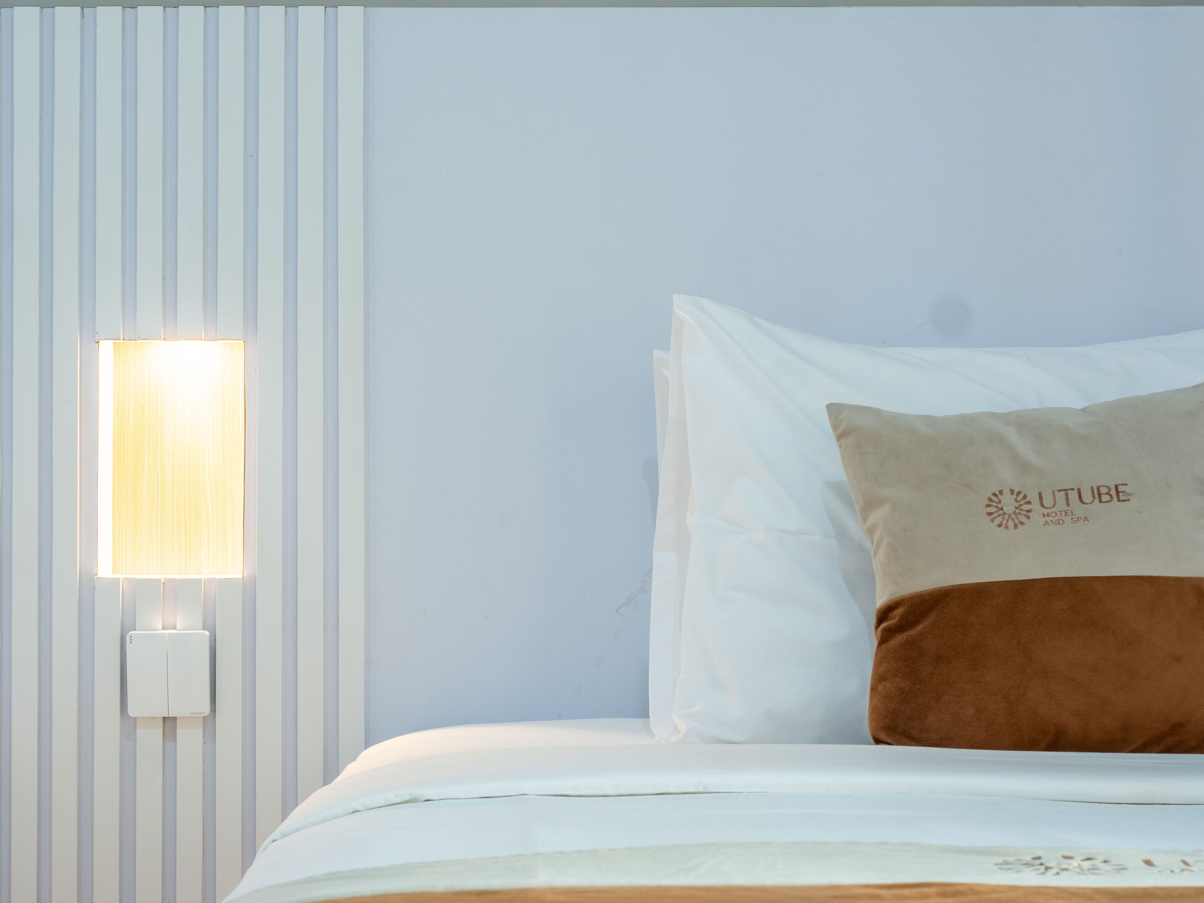 Quarto de hotel com cama, luz acoplada à parede e travesseiro com logótipo.