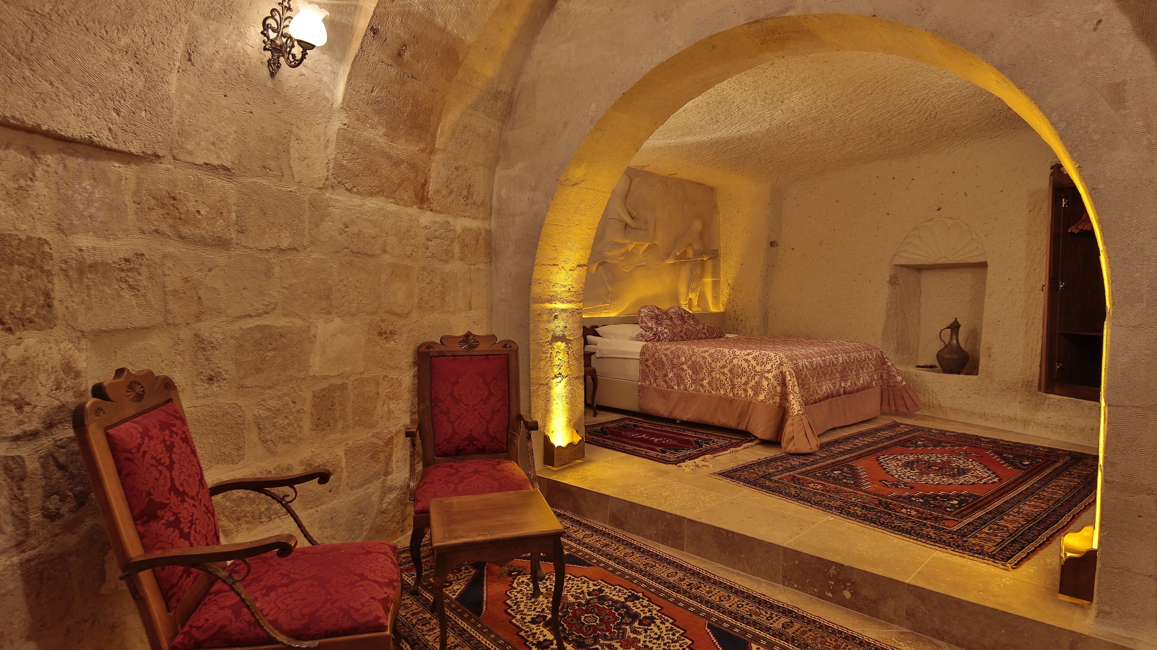 Una habitación con pared de piedra, una silla de madera, una cama con ropa de cama estampada y una alfombra.
