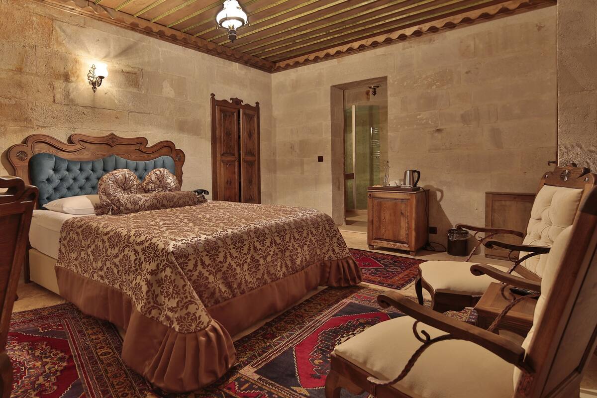 Un dormitorio con una cama grande, cabecera de madera, un armario de madera, una silla y un mueble pequeño.