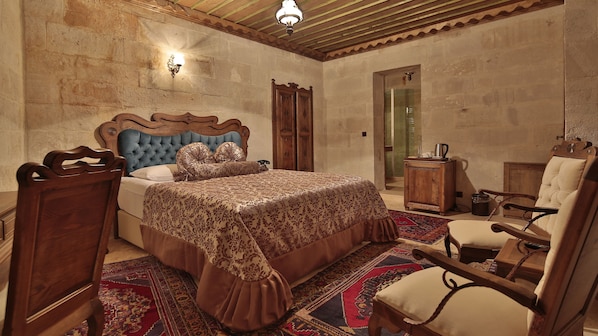 A bedroom with a large bed, wooden headboard, a wooden wardrobe, a chair, and a small cabinet. - Phocas Cave Suites - Special Class (Avanos)