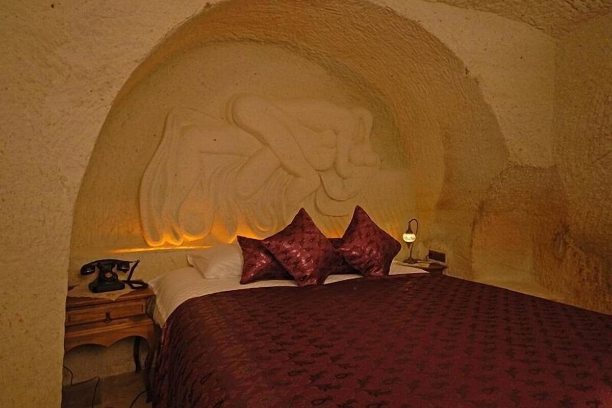 Una habitación con cama, mesita de noche, lámpara y un relieve en la pared.
