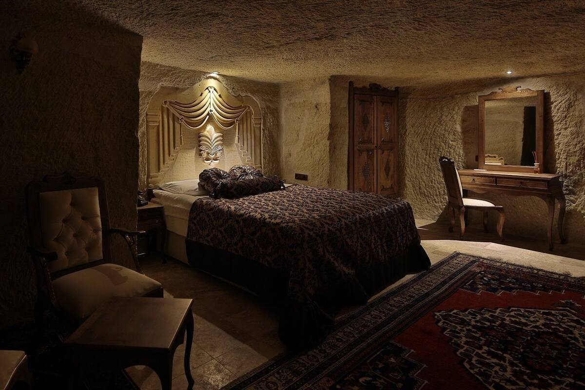 Un dormitorio con poca luz, que incluye una cama grande, una silla, un escritorio y un espejo.