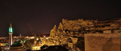 Una vista nocturna de un pueblo histórico con una torre destacada y edificios sobre un terreno montañoso.