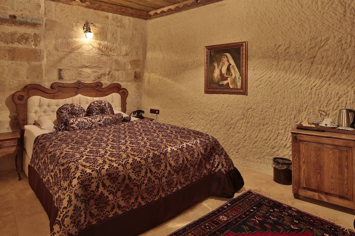 Un dormitorio con una cama grande, un cabecero de madera, una mesita de noche, un aparador de madera, un cuadro en la pared y una pared de piedra.