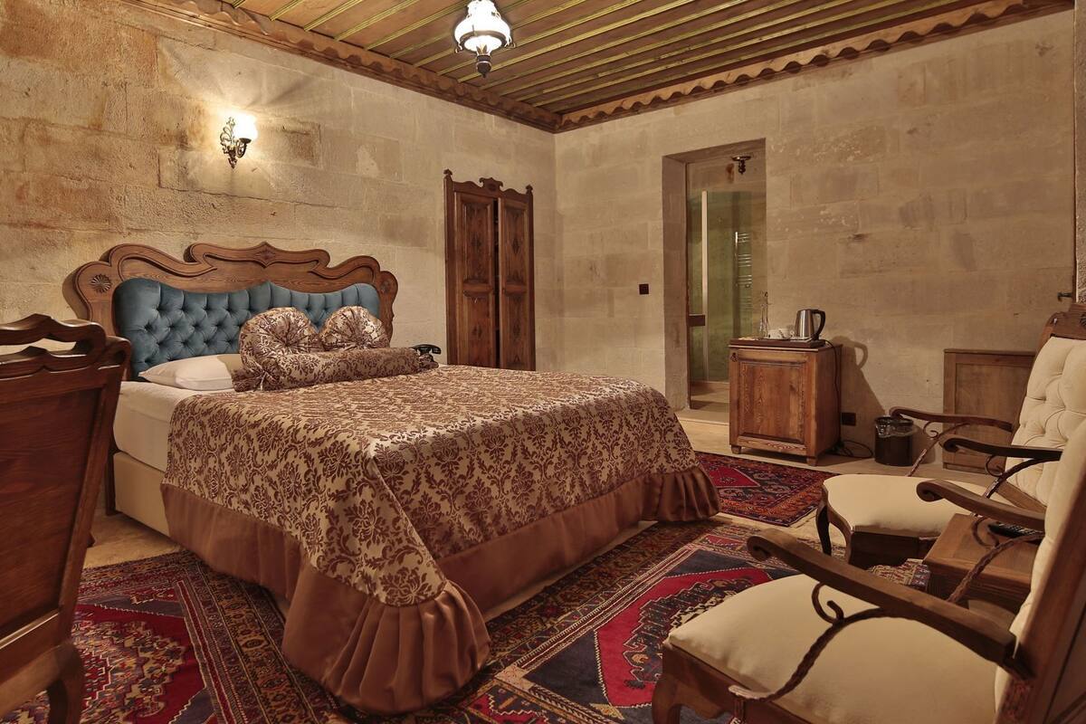 Un dormitorio con una cama grande, cabecera de madera, una mesita de noche, una silla y un armario.