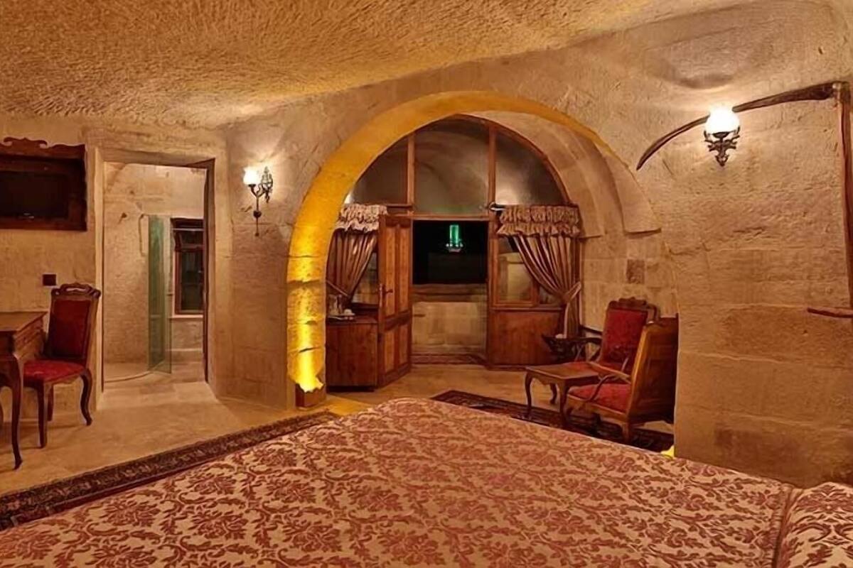 Una habitación con una cama, un escritorio y una silla, con paredes de piedra y un arco de entrada.