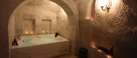 Un cuarto de spa con una bañera grande, paredes de piedra y techo de madera.