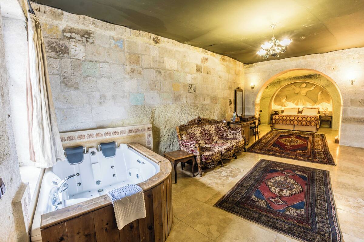 Una habitación con pared de piedra, una bañera de madera, un sofá estampado y una alfombra grande.