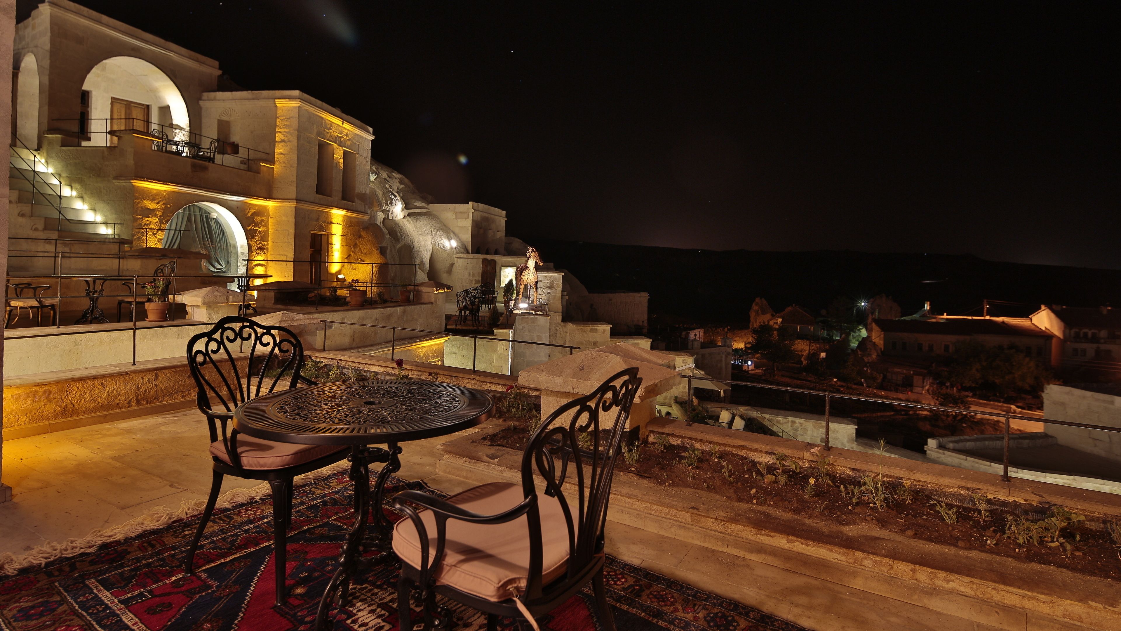 Una terraza al aire libre con una mesa y sillas de piedra, un banco de piedra y vistas a un edificio histórico de noche.