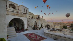 A courtyard with a large rug, potted plants, and a statue. - Phocas Cave Suites - Special Class (Avanos)