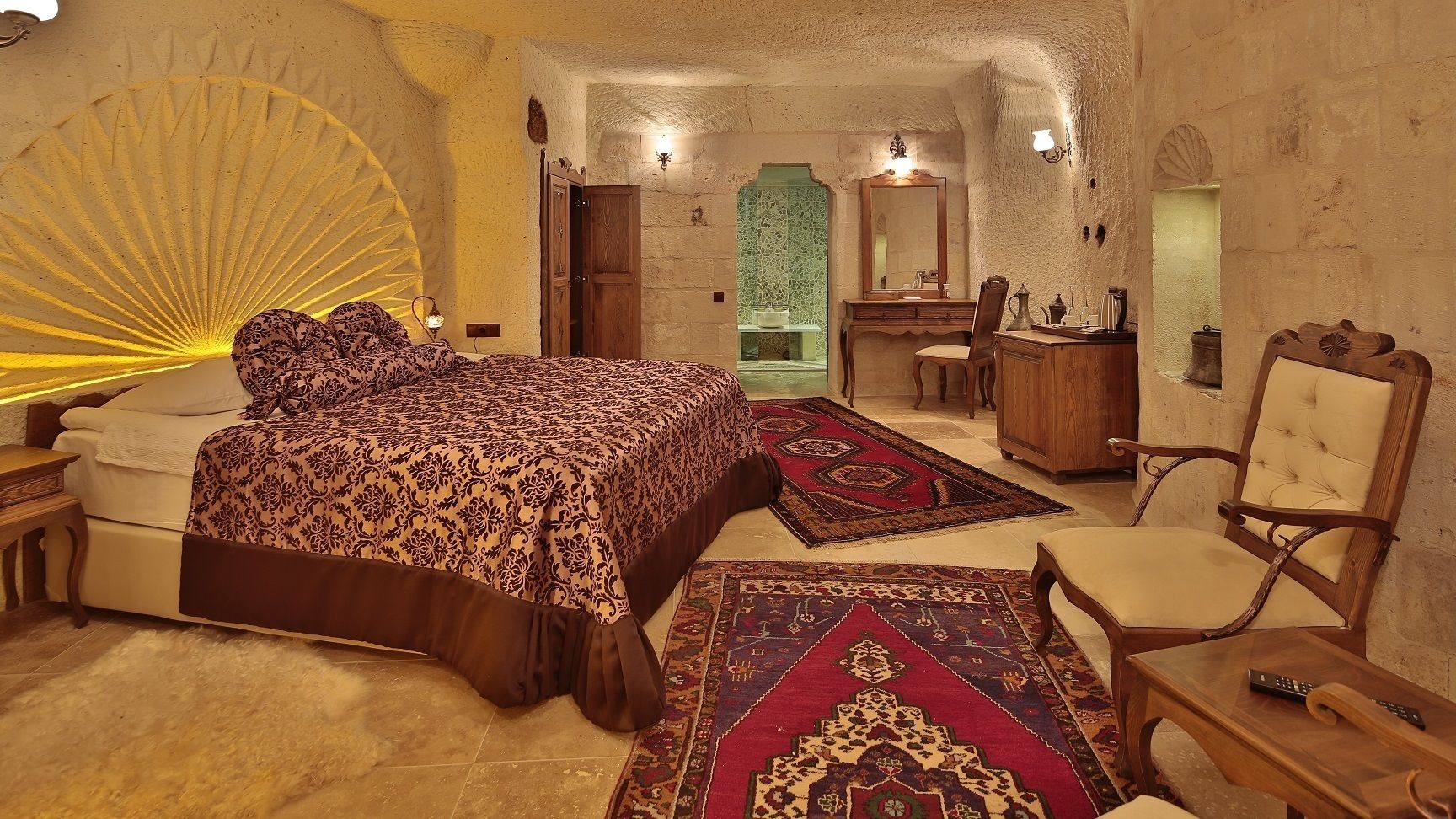 A bedroom with a large bed, a wooden dresser, a chair, and a desk.