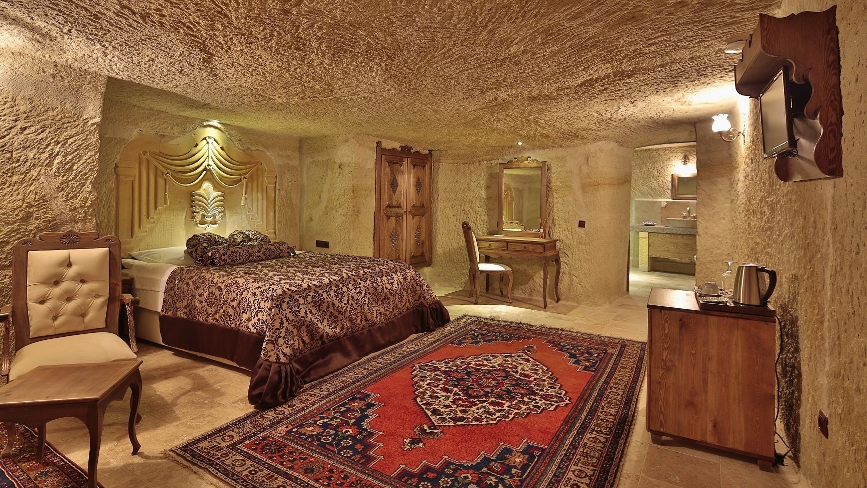 A bedroom with a large bed, a chair, a desk, and a mirror.