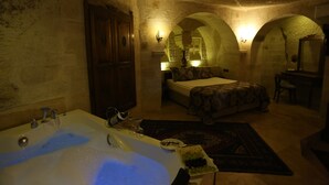 A dimly lit room with a bathtub, a bed, and a desk. - Phocas Cave Suites - Special Class (Avanos)