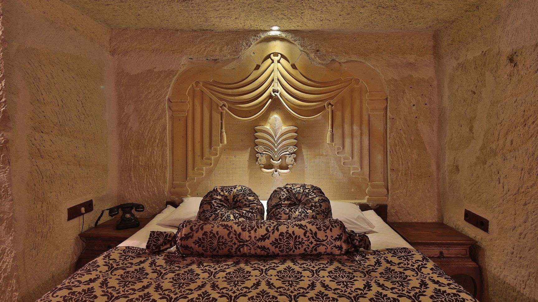 A bedroom with a large bed, a decorative headboard, and a nightstand with a telephone.