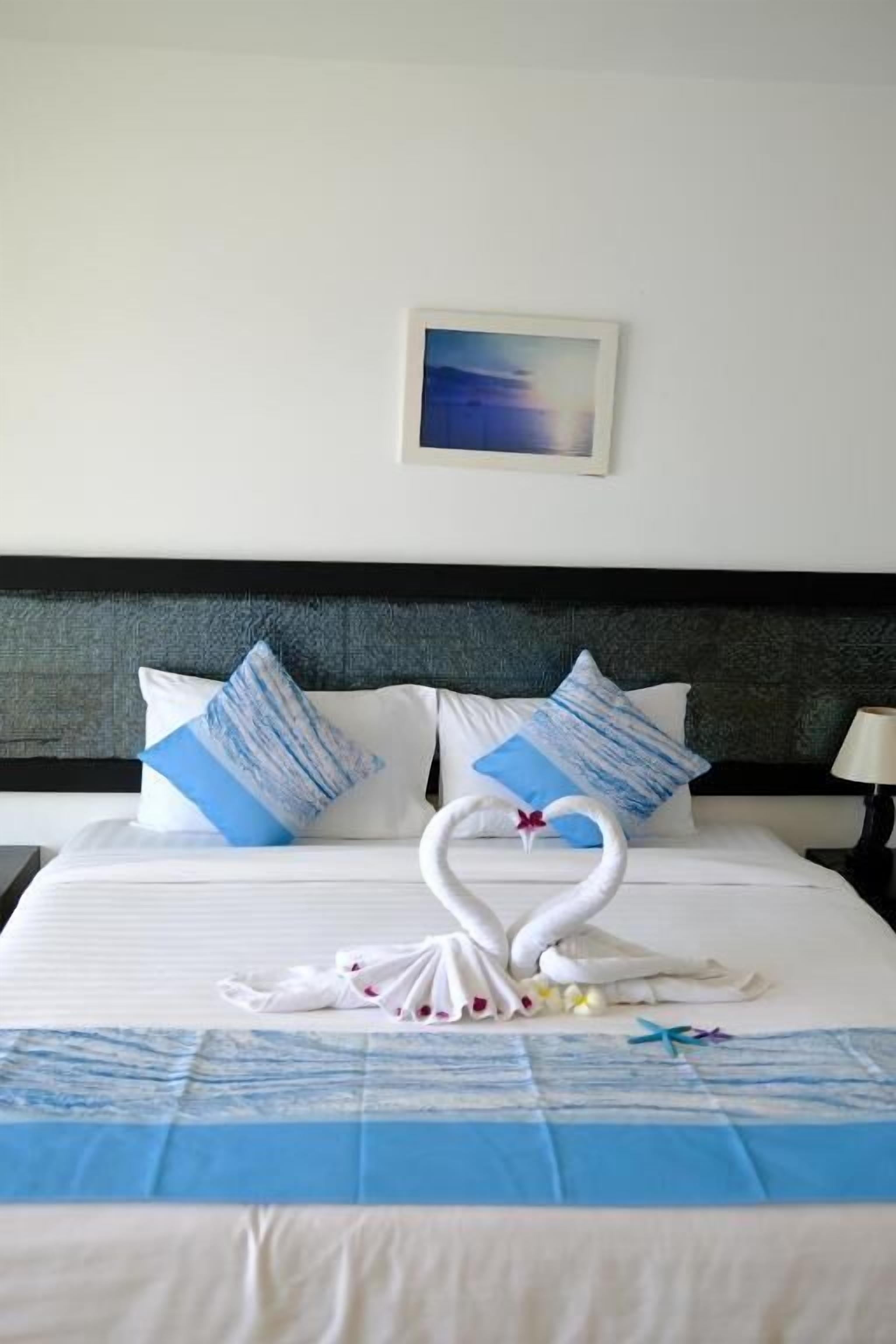 A hotel room with a neatly made bed, a swan-shaped towel arrangement, and a framed picture on the wall.