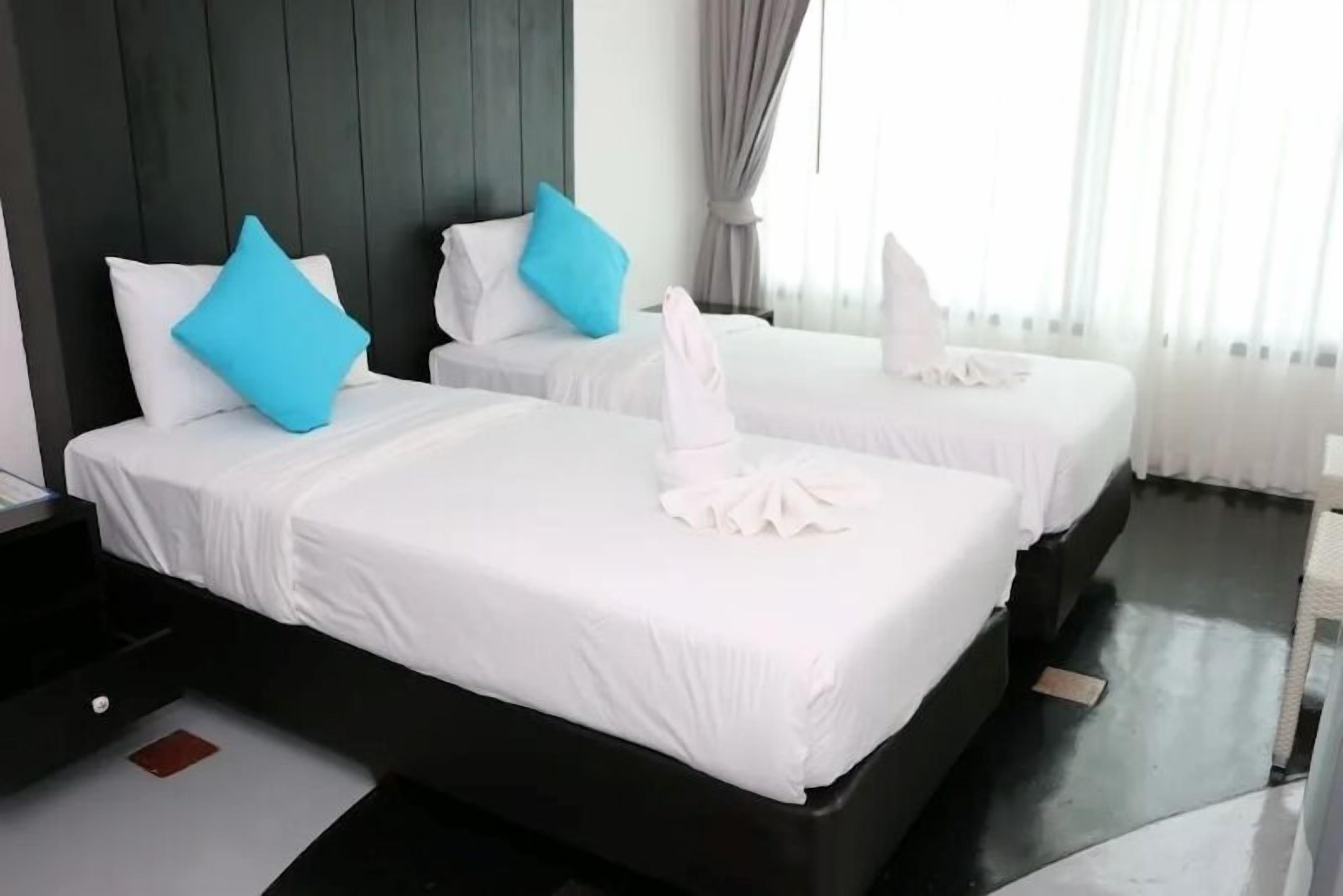 Two beds with white linens and blue pillows, a dark headboard, and a window with curtains.
