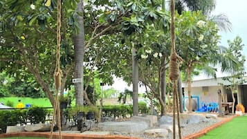 A covered outdoor area with artificial grass, a swing set, and a variety of trees.