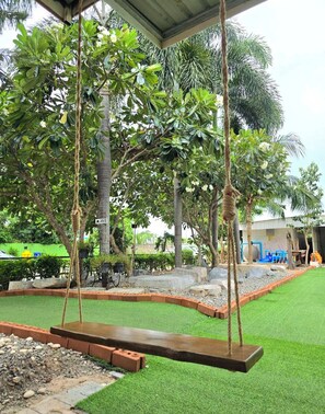 A covered outdoor area with artificial grass, a swing set, and a variety of trees. - The Regizt Hotel Pattaya (Pattaya)