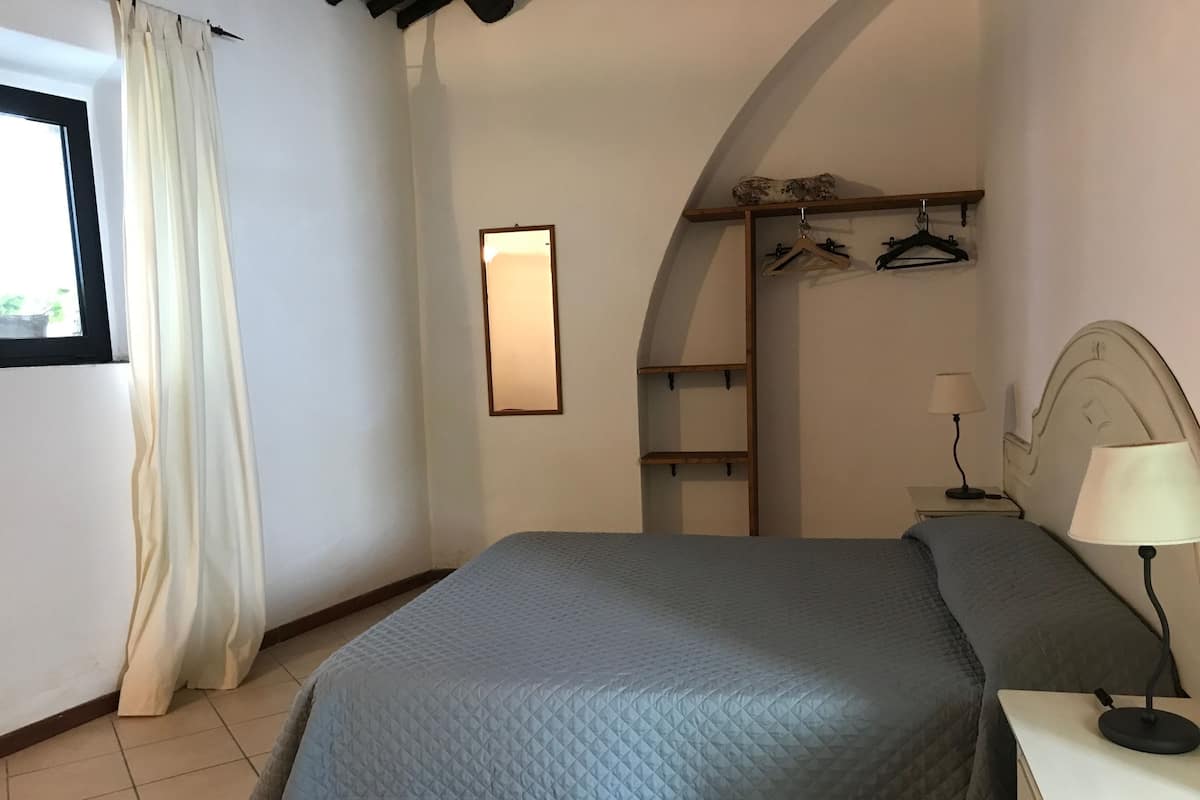 Une chambre à coucher avec un lit, une table de chevet avec une lampe, une armoire et un miroir au mur.