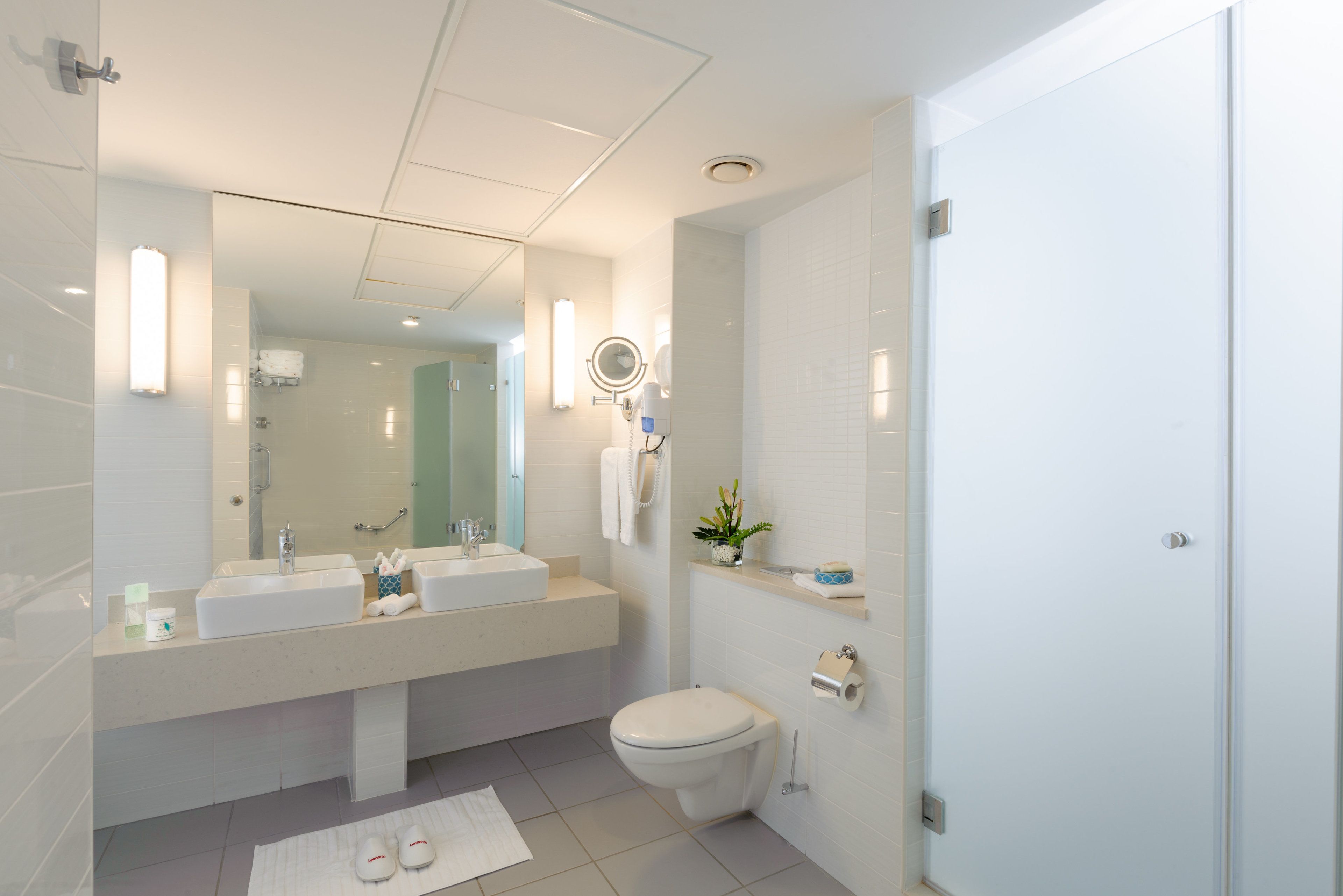 Un baño moderno con un espejo grande, dos lavamanos, inodoro y zona de ducha.